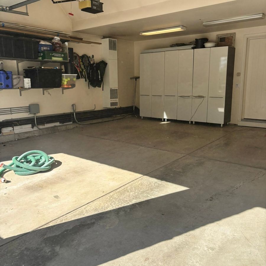 Before epoxy: stained bare concrete garage floor with white storage cabinets